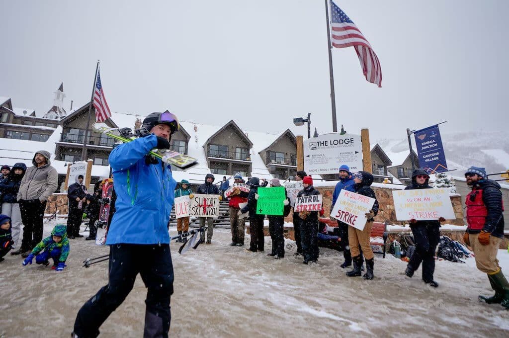 Patrollers striking whilst skiers walk to long lift lines.